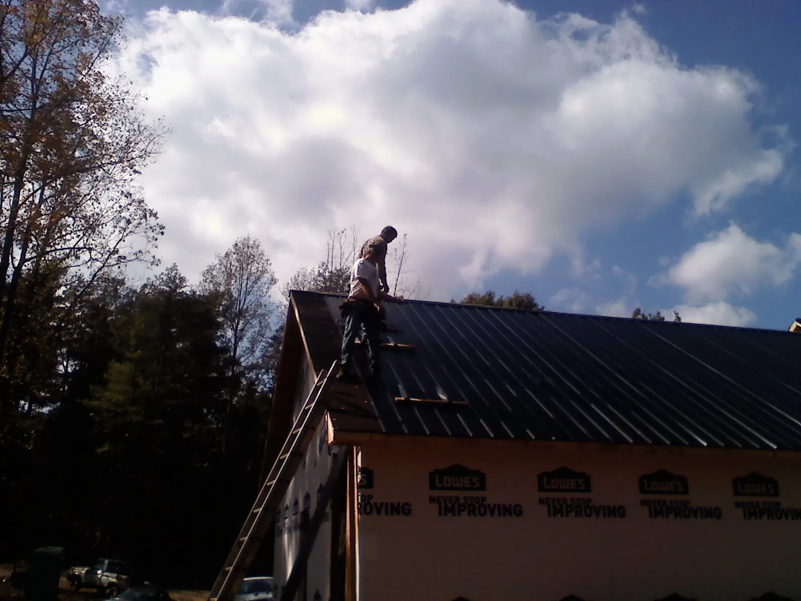 Roofer fastening dark metal panels high against a cloudy sky, from a Roof Inspection job in Truro
