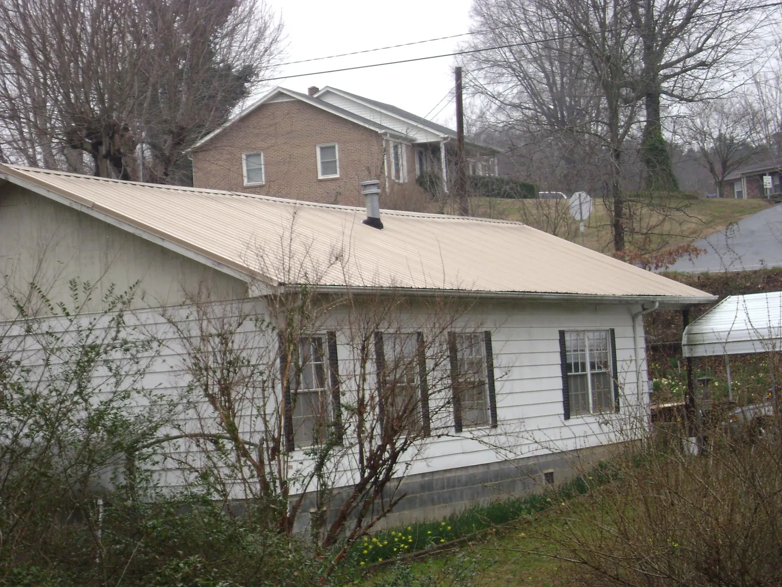 Tan metal roof on a white sided house set into a hillside — Commercial Roofing by Roofing Brothers in Truro